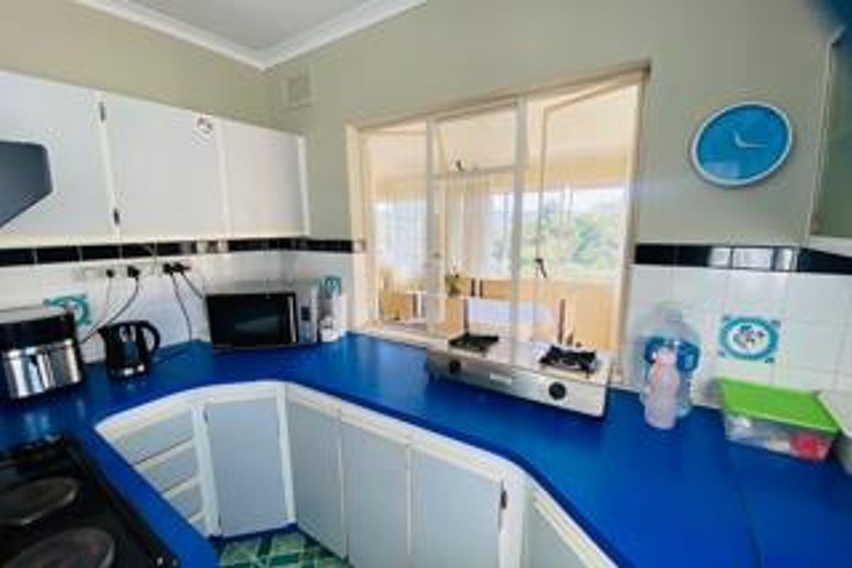A functional kitchen featuring blue countertops, white cabinetry, and a tiled backsplash with a view through the window.