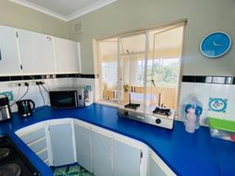 A functional kitchen featuring blue countertops, white cabinetry, and a tiled backsplash with a view through the window.