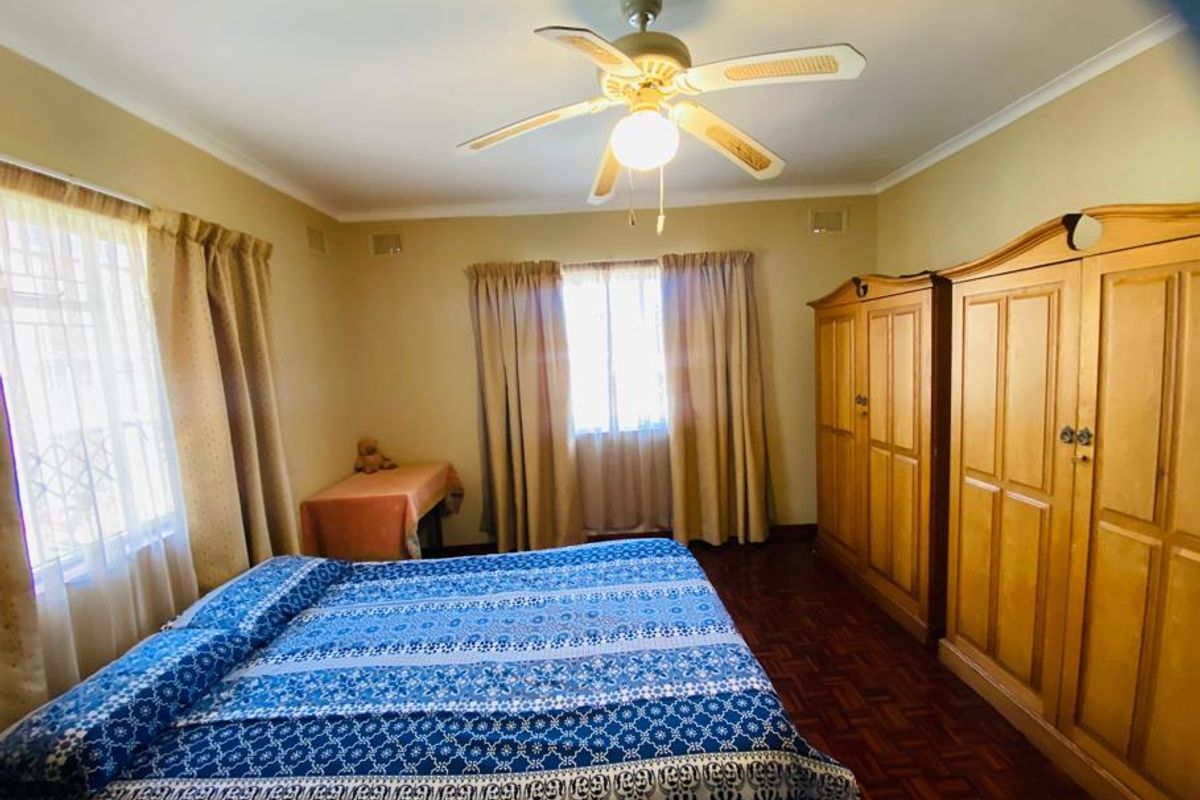 A bedroom featuring parquet flooring, a ceiling fan, and security bars on the windows.