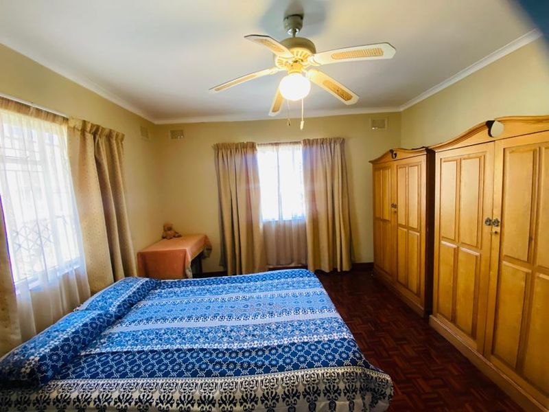 A bedroom featuring parquet flooring, a ceiling fan, and security bars on the windows.