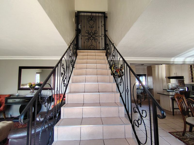 Open plan living area featuring a central tiled staircase with wrought iron balustrades, leading to an upper level, adjacent to a functional kitchen space.