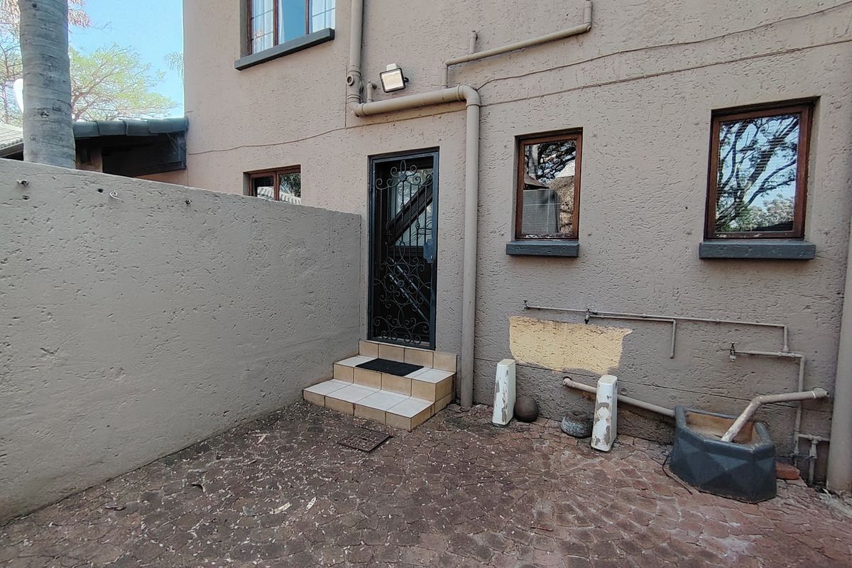 Rear exterior courtyard area featuring a security gate, tiled steps, and exposed exterior plumbing against a textured wall finish.
