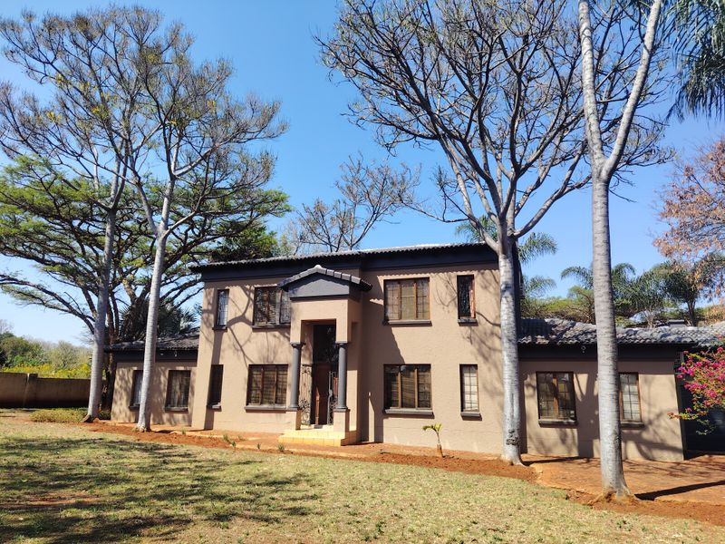 A two-story residential home featuring a stucco facade, a covered entrance portico with decorative columns, and mature trees in the front garden.