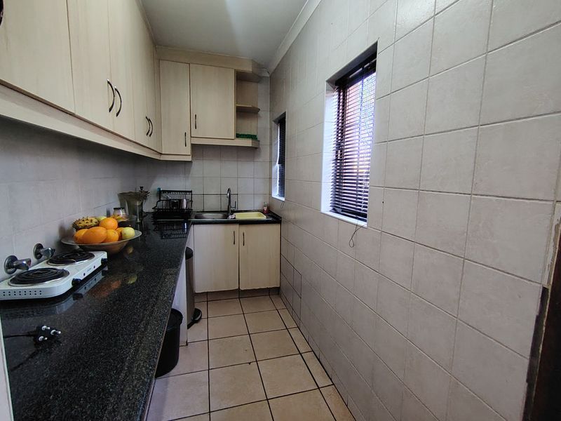 A functional scullery featuring granite countertops, built-in cabinetry, tiled walls, and tiled flooring, providing additional prep and wash-up space.