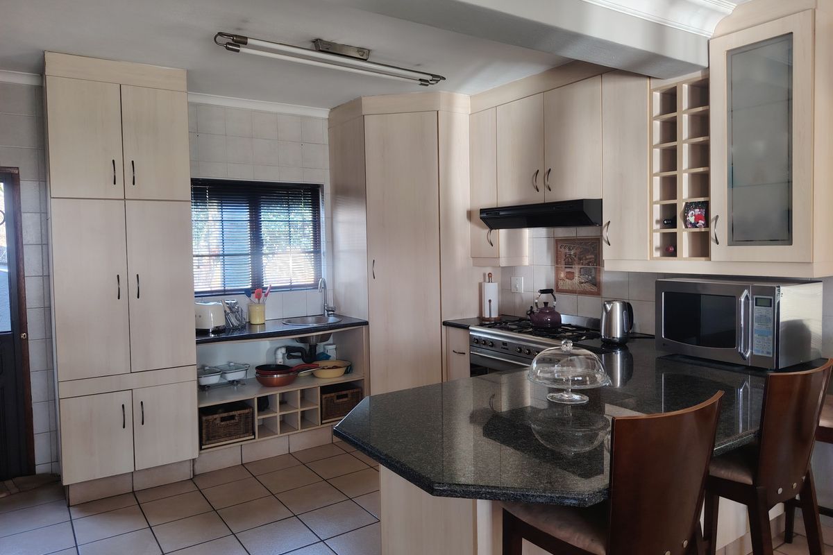A functional kitchen featuring light-toned built-in cabinetry, granite countertops, a gas hob with extractor, and tiled flooring with a breakfast bar area.