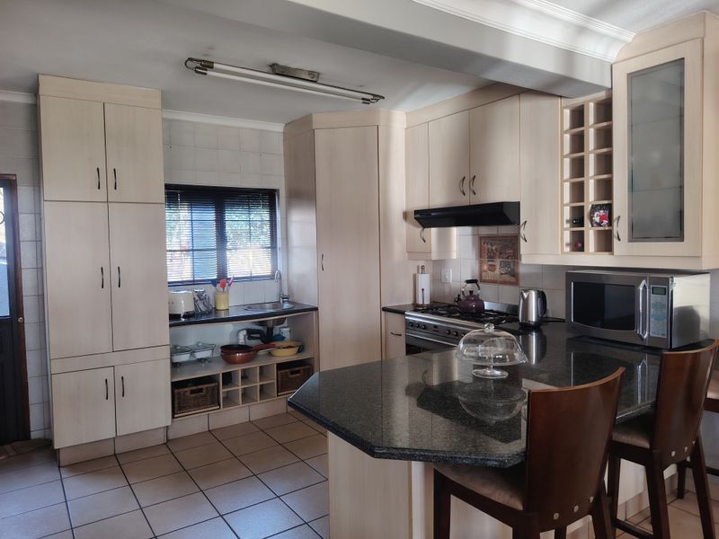 A functional kitchen featuring light-toned built-in cabinetry, granite countertops, a gas hob with extractor, and tiled flooring with a breakfast bar area.