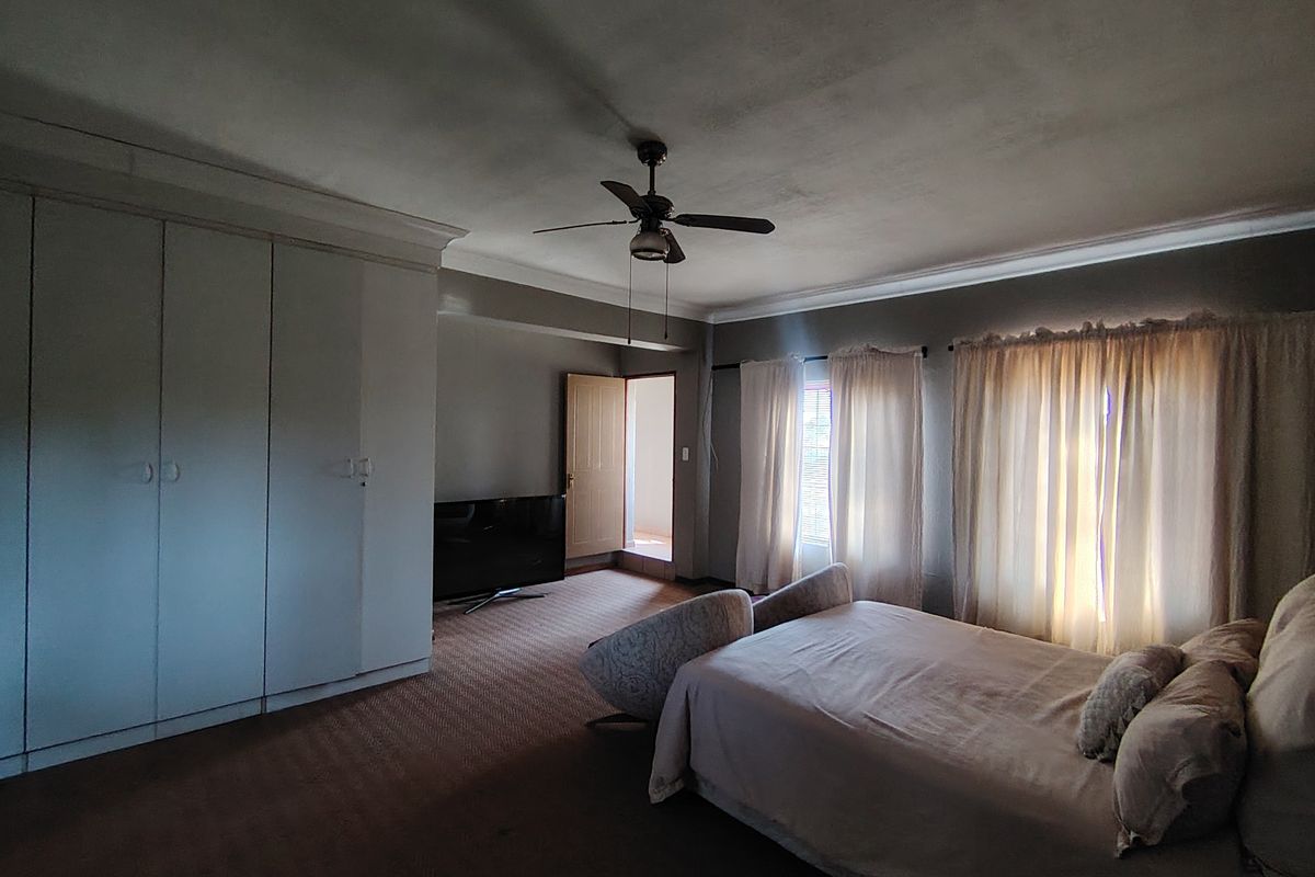 Spacious bedroom featuring built-in cupboards, a ceiling fan, and carpeted flooring. The room offers ample space and natural light through window curtains.