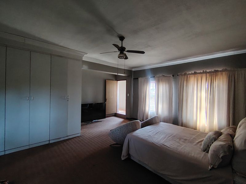 Spacious bedroom featuring built-in cupboards, a ceiling fan, and carpeted flooring. The room offers ample space and natural light through window curtains.