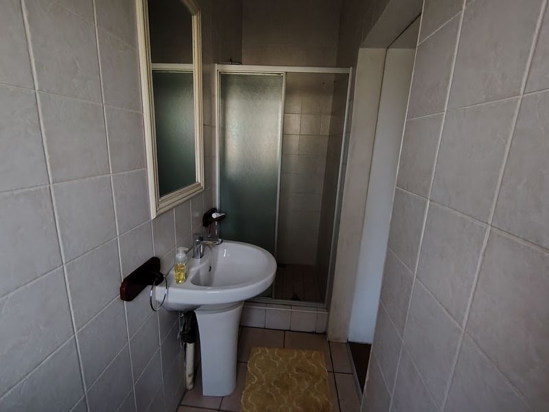 A functional bathroom featuring a pedestal basin, a shower enclosure, and neutral wall and floor tiling.