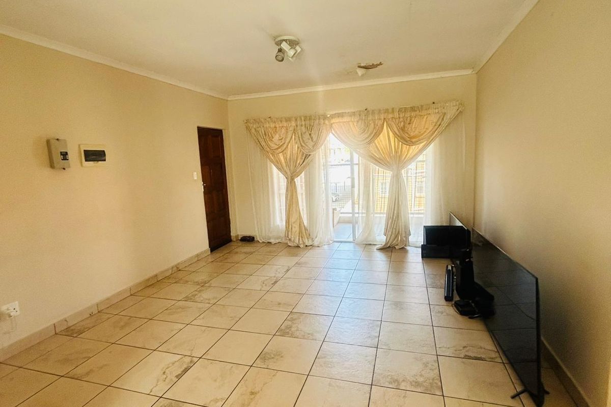 A spacious, empty living room featuring neutral tiled flooring, a sliding glass door leading to the exterior, and a ceiling-mounted light fixture.