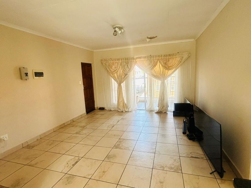 A spacious, empty living room featuring neutral tiled flooring, a sliding glass door leading to the exterior, and a ceiling-mounted light fixture.