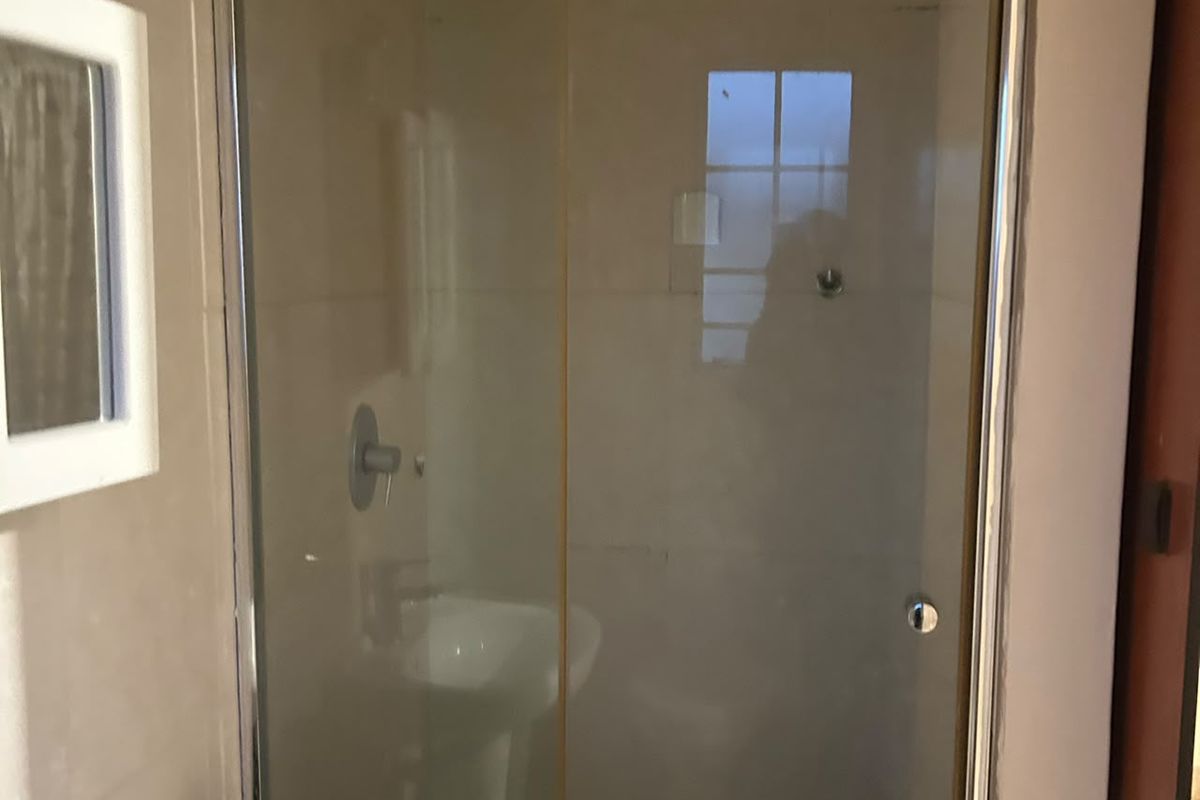 A functional bathroom featuring a glass-enclosed shower, pedestal basin with mixer tap, and wall-mounted storage cabinet with tiled finishes.