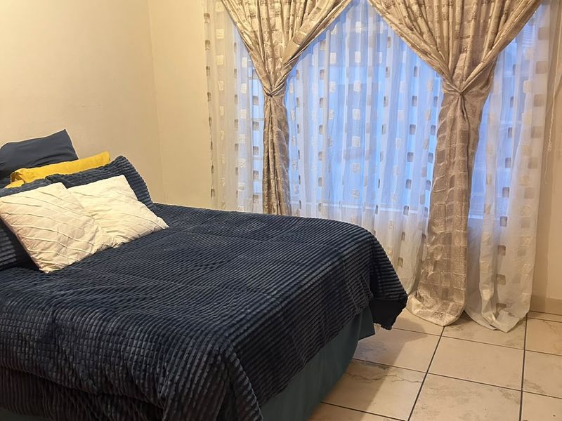 A bedroom featuring tiled flooring and window treatments. The space is functional but would benefit from cosmetic updates to the flooring and finishes.