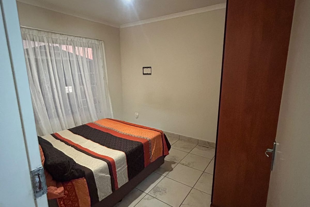 A functional bedroom featuring tiled flooring, a built-in wardrobe, and natural light through a window with curtains.