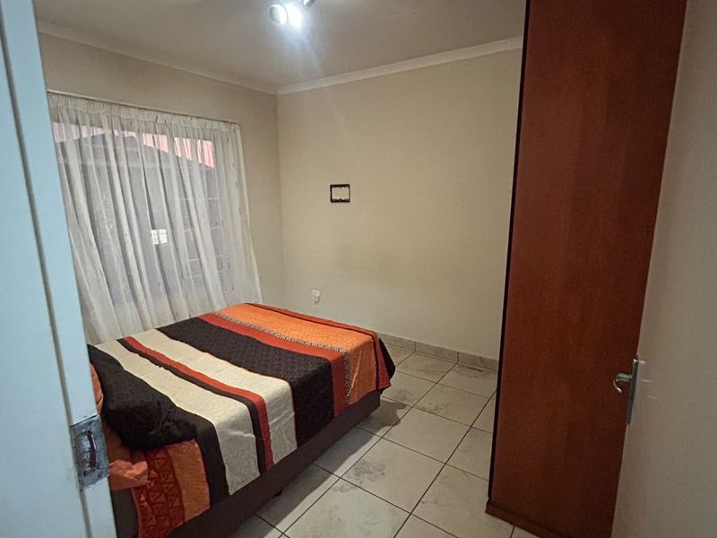 A functional bedroom featuring tiled flooring, a built-in wardrobe, and natural light through a window with curtains.