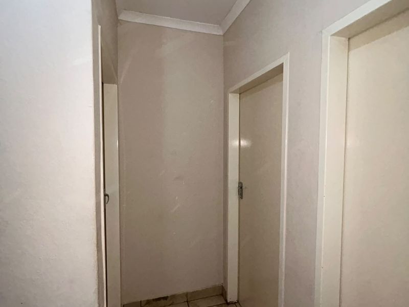 A narrow interior hallway featuring tiled flooring and multiple internal doors, showing signs of wear and requiring cosmetic updates.