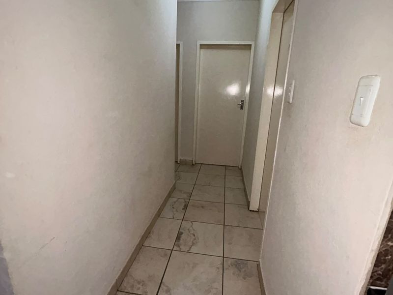 A narrow residential hallway featuring ceramic floor tiles and access to multiple rooms via standard interior doors.