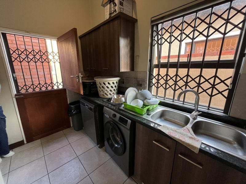 Functional laundry area featuring built-in cabinetry, double stainless steel sink, tiled flooring, and secure window and door access.