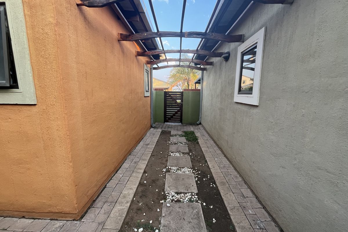 A narrow side passage featuring a timber pergola structure, paved walkway with stepping stones, and a rear timber gate.