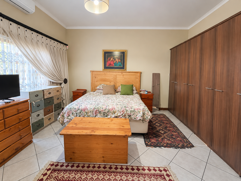 A well-maintained bedroom featuring large built-in wardrobes, tiled flooring, and a wall-mounted air conditioning unit.