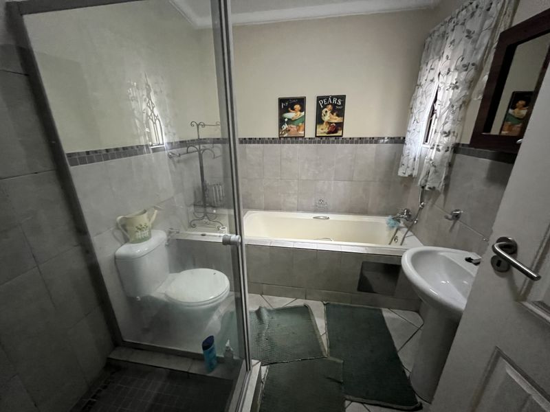A functional bathroom featuring a shower enclosure, bathtub, pedestal basin, and toilet with neutral wall tiling.