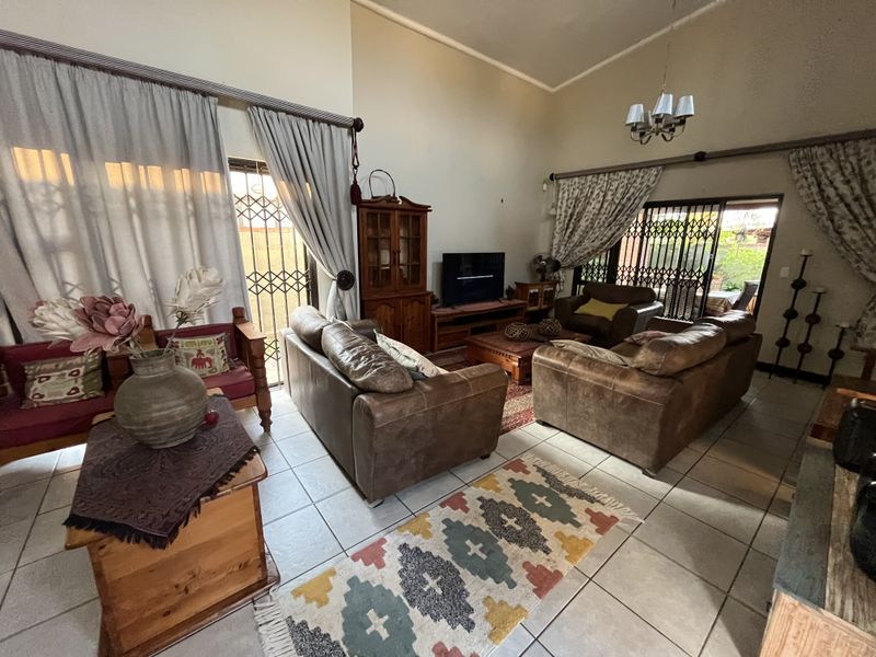 Spacious living room featuring high vaulted ceilings, tiled flooring, and large sliding glass doors with security gates providing access to the outdoor area.