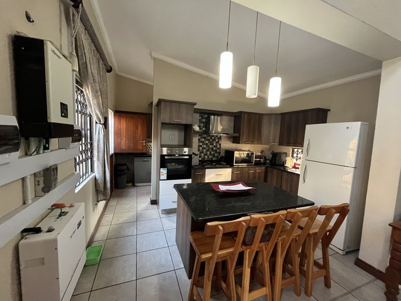 A functional kitchen featuring dark wood cabinetry, granite countertops, a central island, and integrated solar power infrastructure, finished with tiled flooring.
