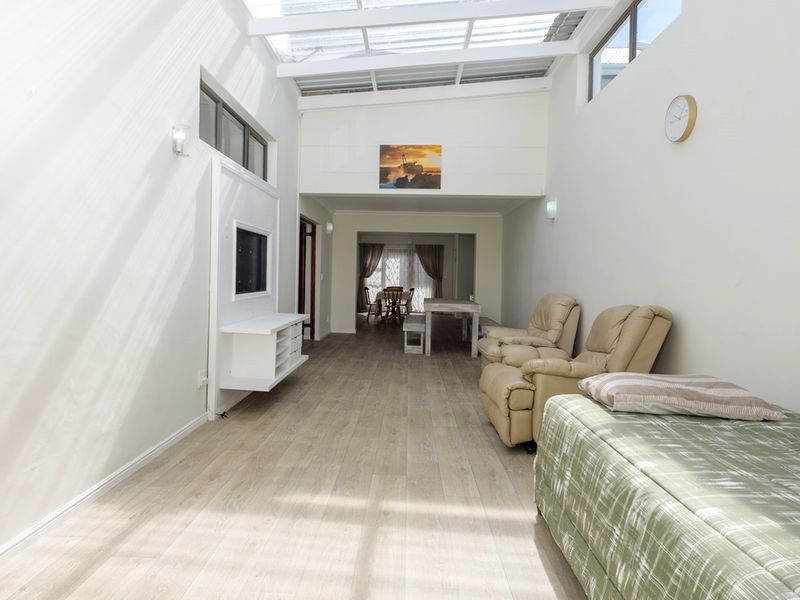 Spacious open-plan living area featuring light laminate flooring, a built-in media unit, and a bright, translucent roof panel design.