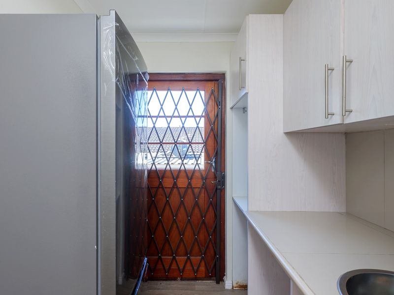 A functional scullery area featuring built-in cabinetry, a laminate countertop with a stainless steel sink, and a secure timber door with a security gate.
