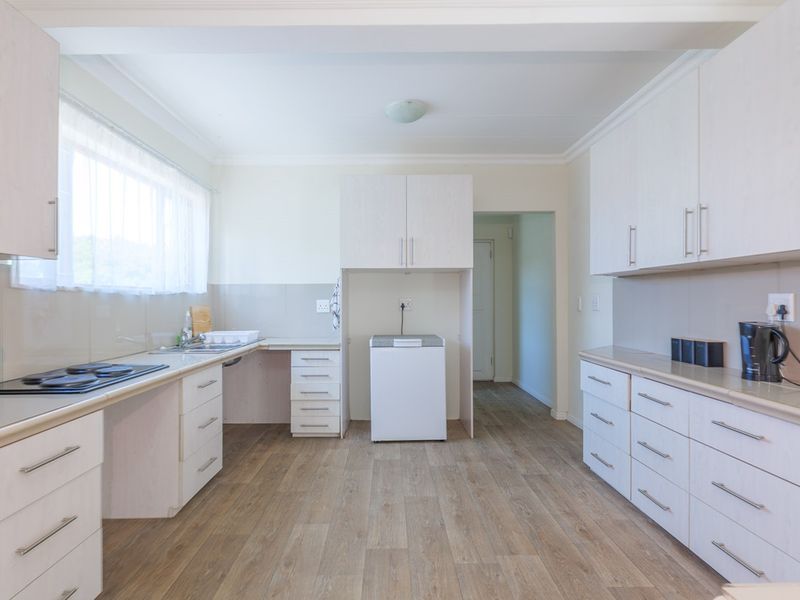 A functional kitchen featuring light-toned cabinetry, laminate countertops, integrated oven and hob, and durable laminate flooring with ample storage space.
