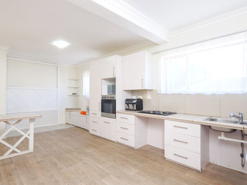 A bright, empty kitchen featuring white built-in cabinetry, laminate countertops, a built-in oven, and a stainless steel sink with tiled backsplash.