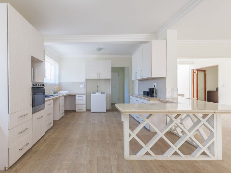 Spacious kitchen featuring light-toned built-in cabinetry, tiled countertops, a breakfast bar, and wood-look laminate flooring in an open-plan layout.