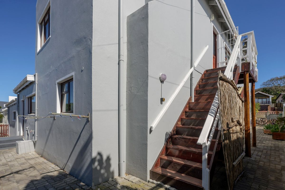 Rear exterior view of the property featuring a paved courtyard and an external timber staircase leading to an upper level.
