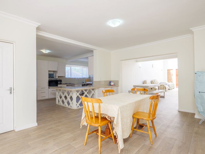 Spacious open-plan living and dining area featuring light laminate flooring, crown molding, and a functional kitchen with built-in cabinetry and appliances.