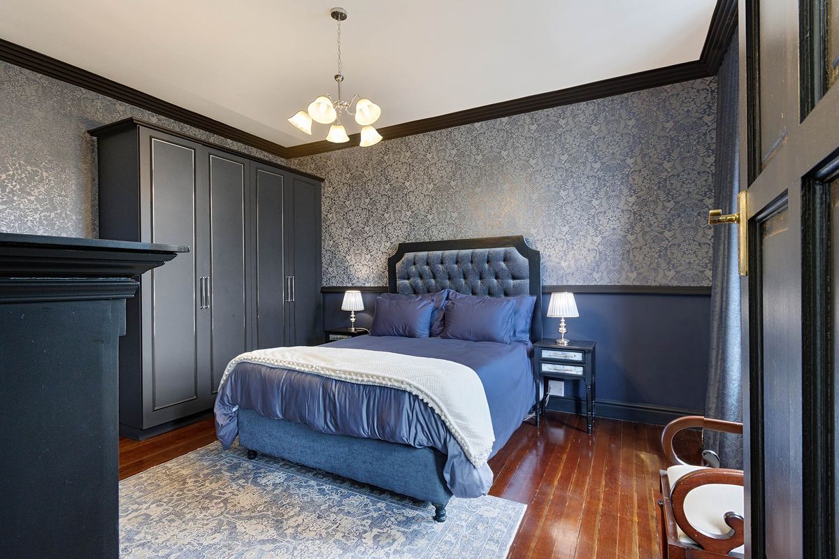 A well-maintained bedroom featuring hardwood flooring, crown molding, a built-in wardrobe, and a decorative fireplace mantel.