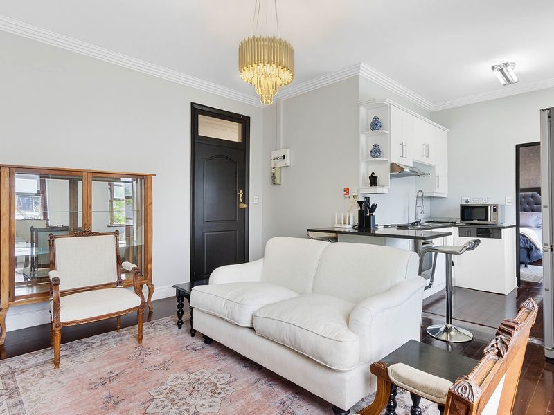 Open-plan living area featuring a modern kitchen with stone countertops, sleek cabinetry, and elegant crown molding, complemented by rich hardwood flooring throughout.