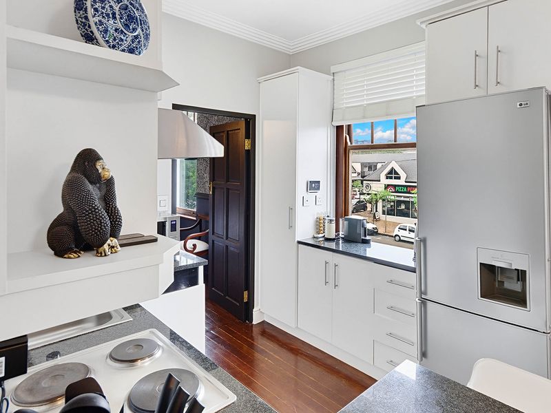 A well-maintained kitchen featuring white cabinetry, stone countertops, electric hob, extractor fan, and polished timber flooring with a view of the street.