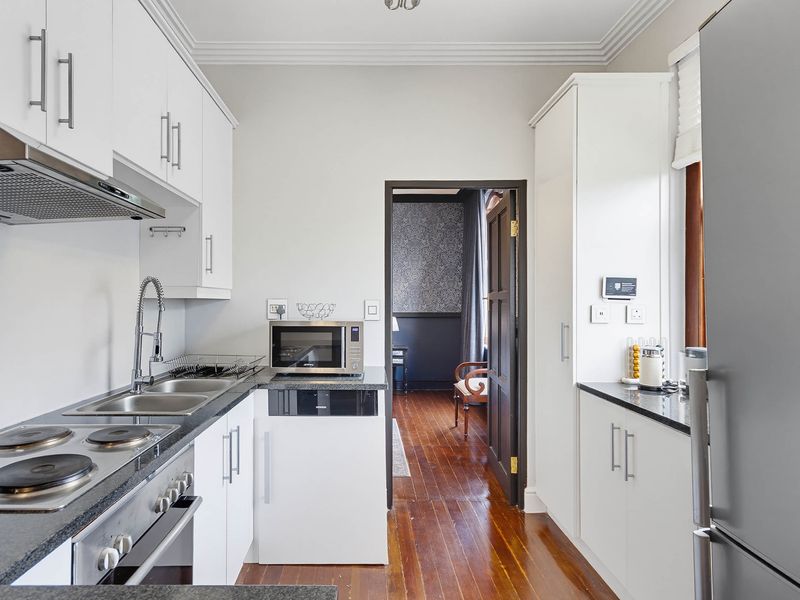 A well-maintained galley kitchen featuring white cabinetry, granite countertops, integrated appliances, and polished hardwood flooring.