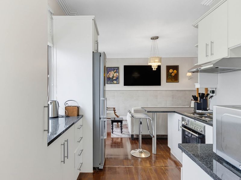 A well-maintained open-plan kitchen and living area featuring modern white cabinetry, granite countertops, stainless steel appliances, and polished hardwood flooring.