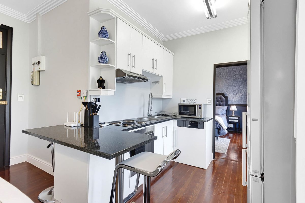 Compact kitchen featuring white cabinetry, granite countertops, an electric hob, and an integrated extractor fan, finished with hardwood flooring and decorative coving.