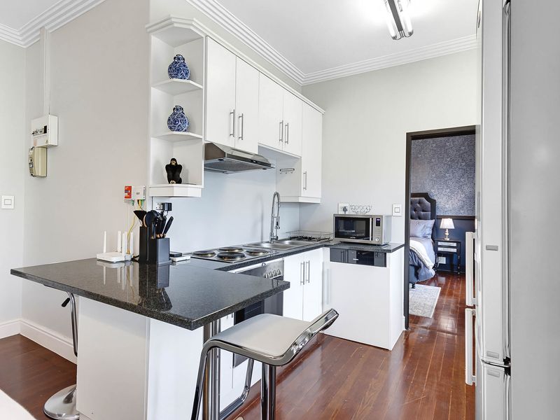 Compact kitchen featuring white cabinetry, granite countertops, an electric hob, and an integrated extractor fan, finished with hardwood flooring and decorative coving.