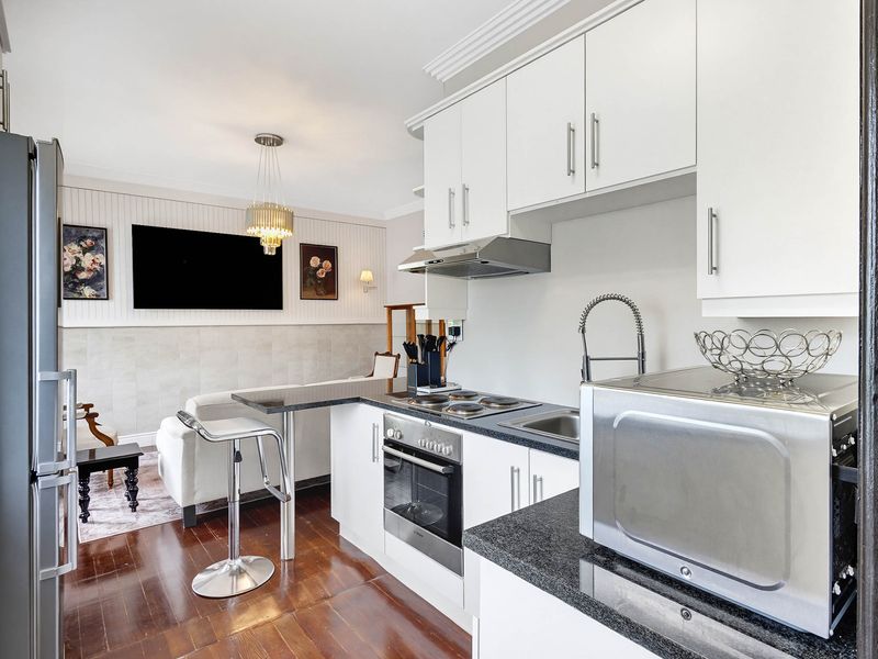Modern open-plan kitchen featuring white cabinetry, granite countertops, and integrated appliances, seamlessly flowing into a cozy living area with hardwood floors and elegant wainscoting.