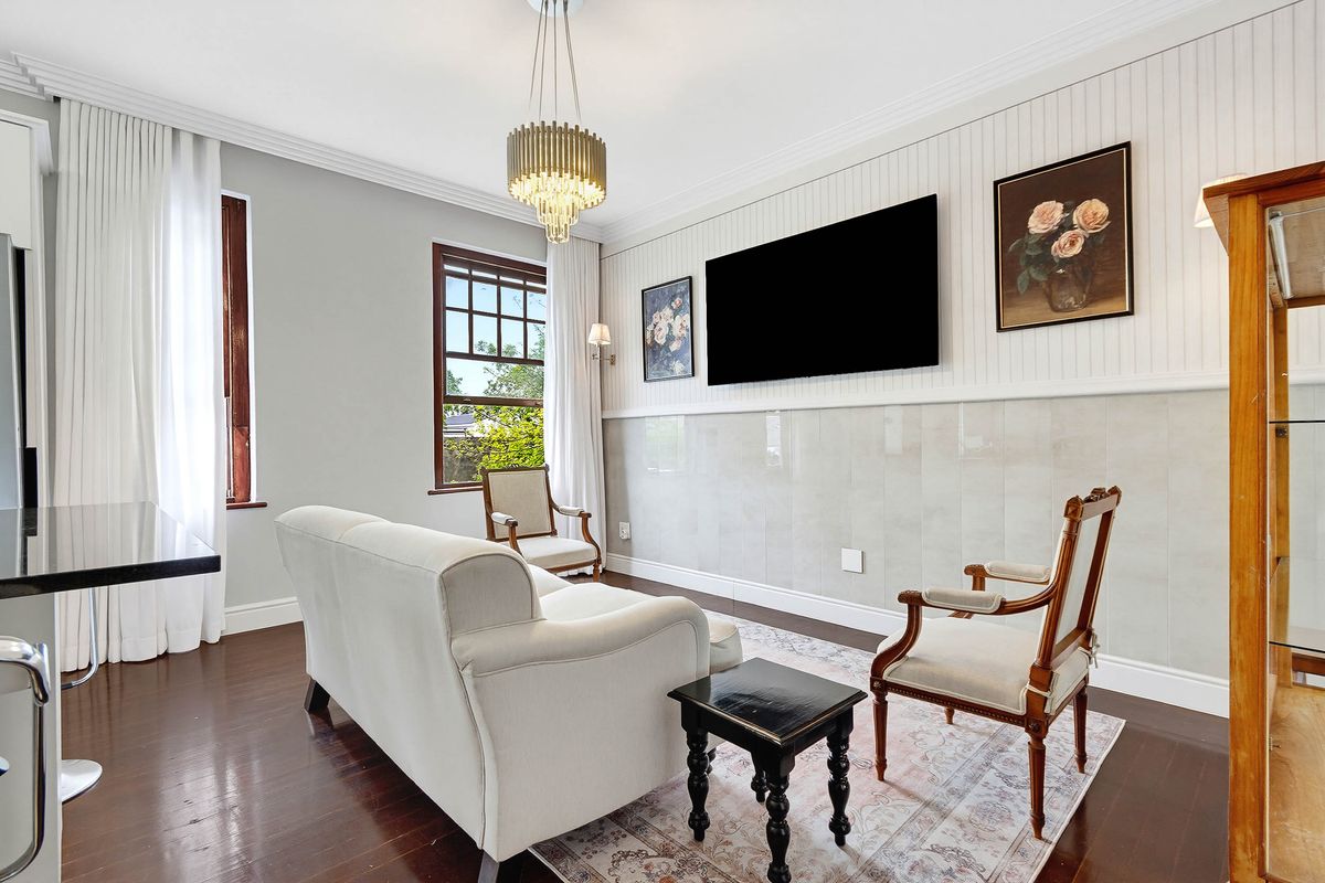 A well-maintained living room featuring hardwood floors, elegant wainscoting, tiled wall accents, and a classic chandelier, offering a refined and comfortable living space.