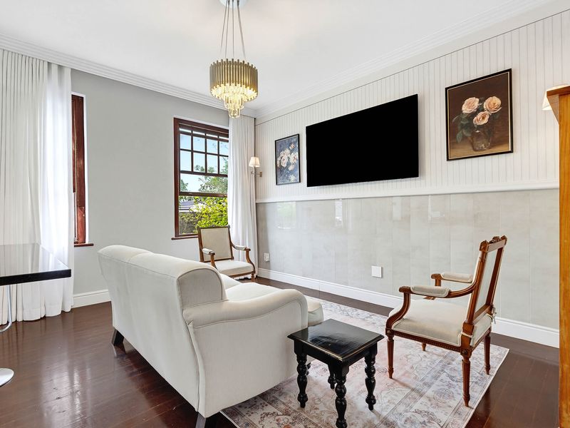 A well-maintained living room featuring hardwood floors, elegant wainscoting, tiled wall accents, and a classic chandelier, offering a refined and comfortable living space.