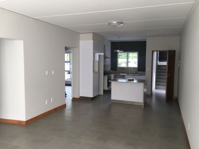 Spacious open-plan living and kitchen area featuring modern tiled flooring, a central kitchen island, and neutral finishes throughout.