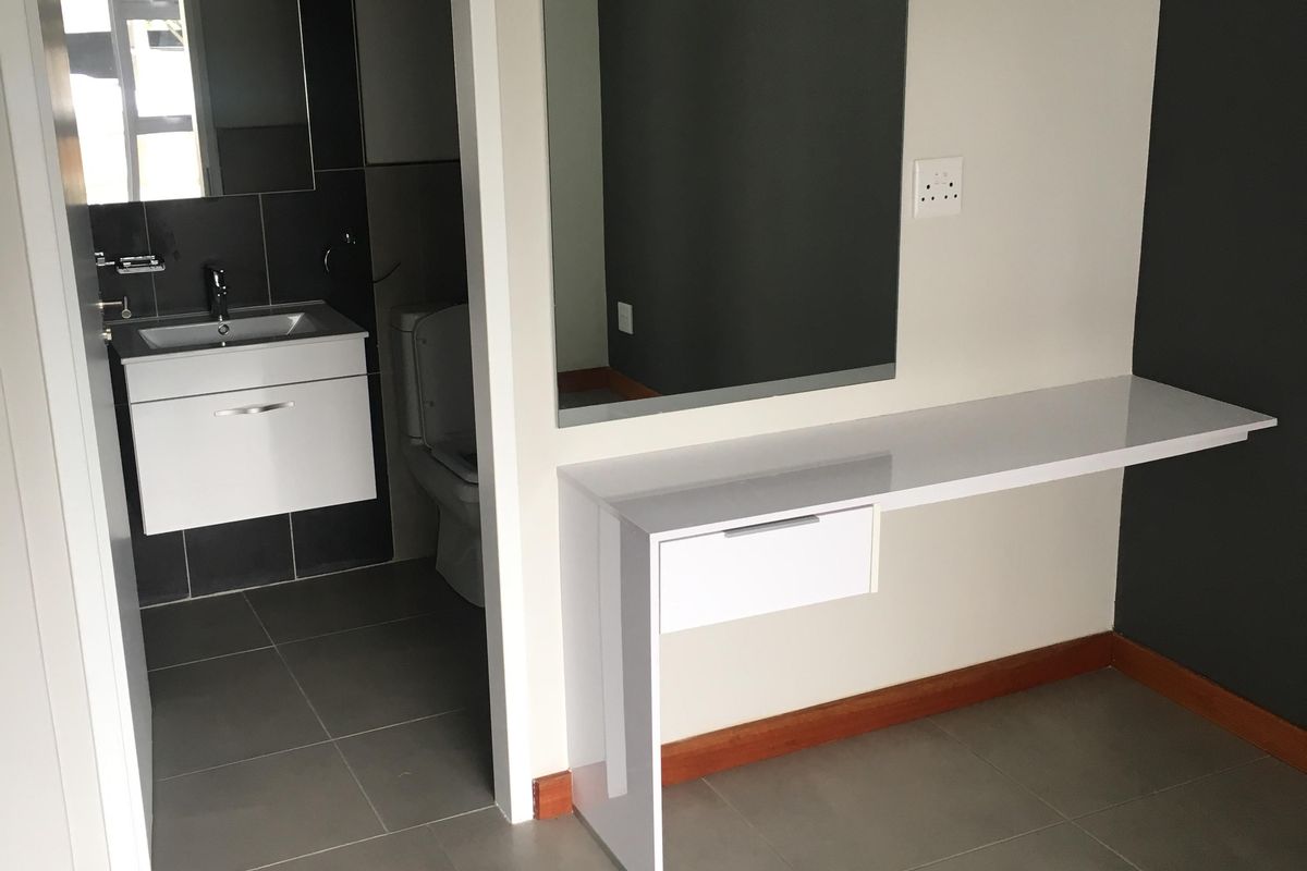A clean bedroom area featuring a modern built-in vanity with a mirror, leading into an en-suite bathroom with contemporary tiling and fixtures.