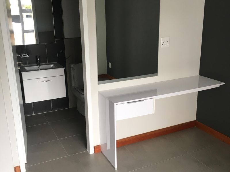 A clean bedroom area featuring a modern built-in vanity with a mirror, leading into an en-suite bathroom with contemporary tiling and fixtures.