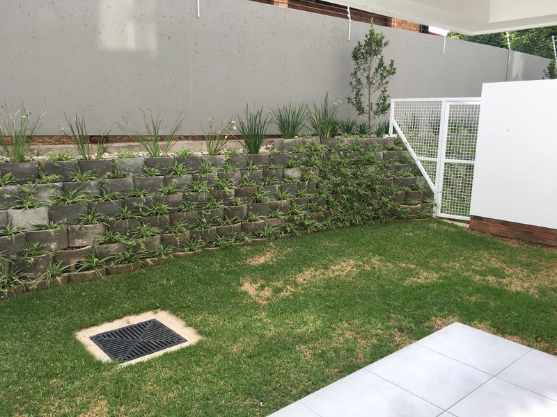 A private garden area featuring a tiered concrete retaining wall with integrated planting, a small lawn, and a paved patio section.
