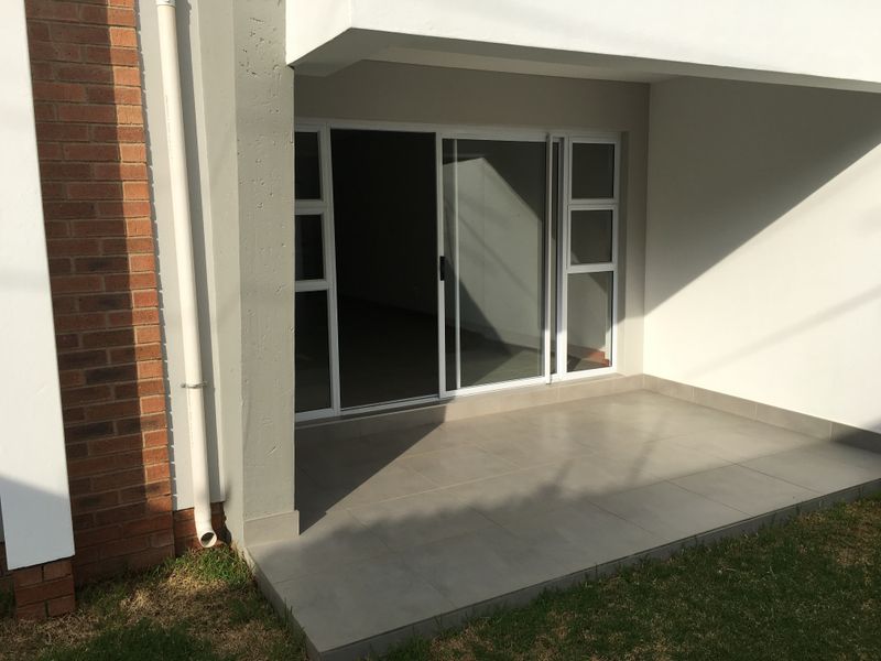 A clean, covered patio area featuring modern floor tiles and a large sliding glass door providing access to the interior living space.