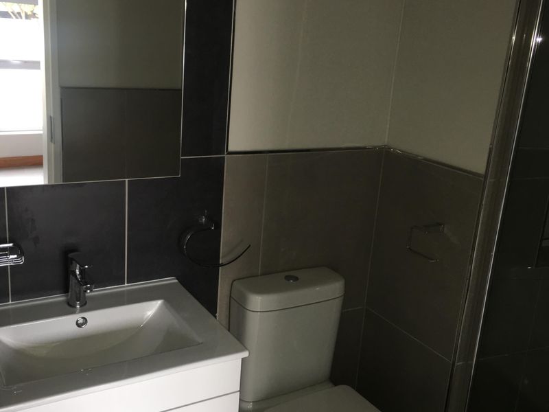 A modern bathroom featuring a vanity cabinet with a ceramic basin, a toilet, and a glass-enclosed shower with neutral wall and floor tiling.